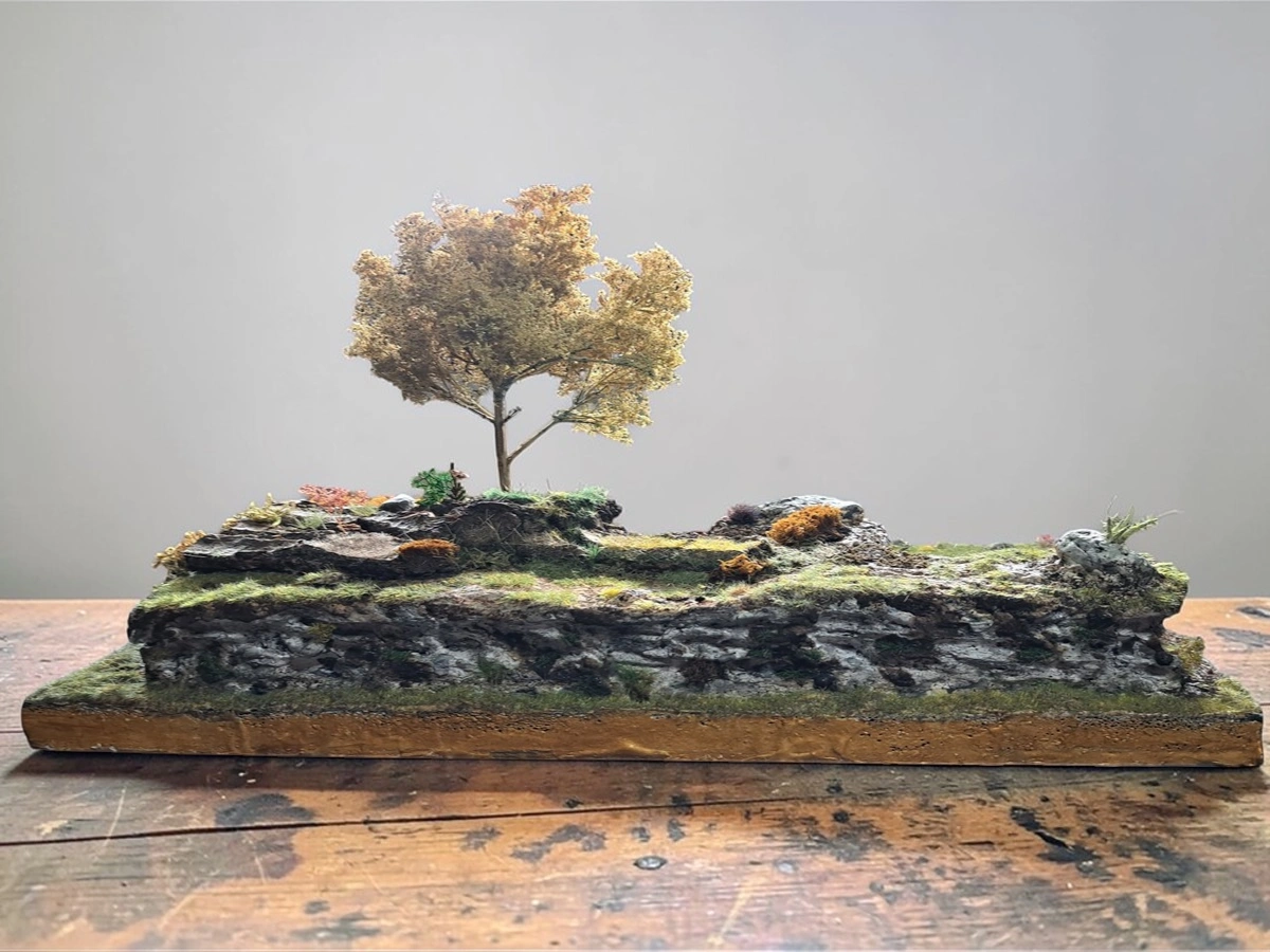 Diorama terreno roccioso realistico con albero autunnale, muschio e vegetazione mista